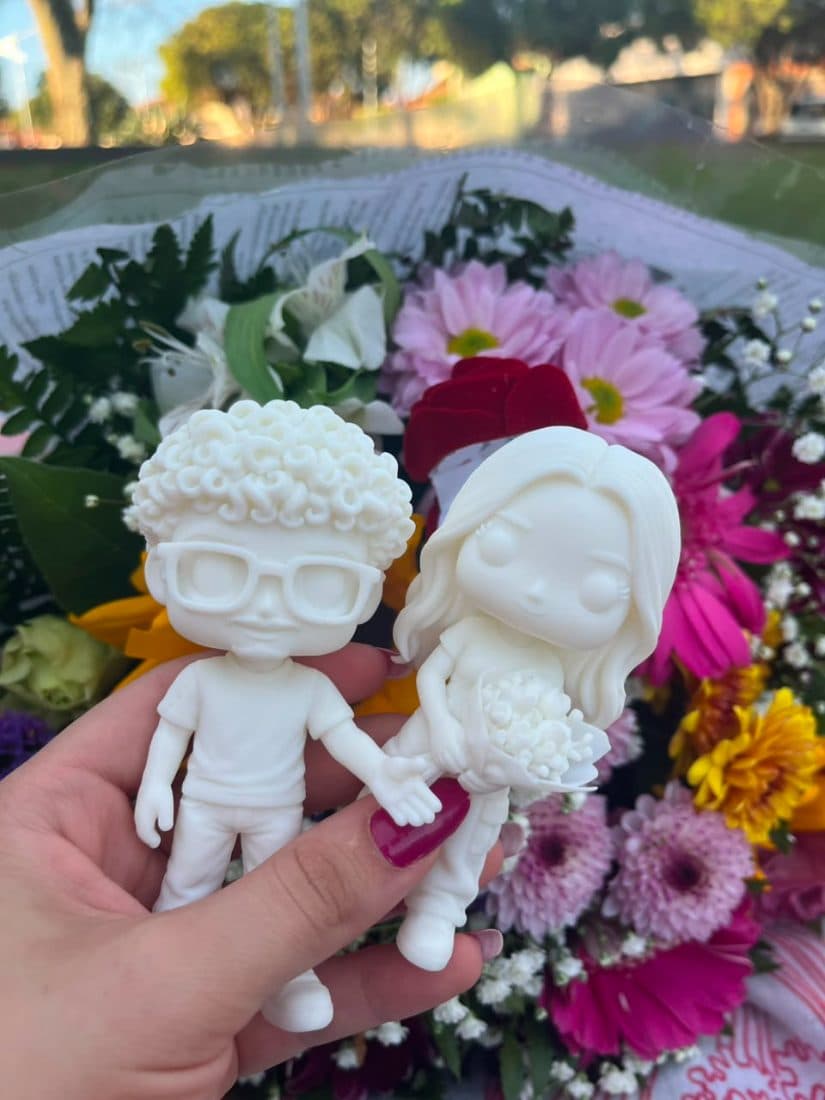 Casal em miniatura segurado na mão, com um buquê de flores ao fundo